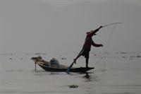 Fisherman paddling with his leg whilst casting his net