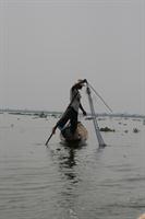 Fisherman paddling with his leg whilst casting his net